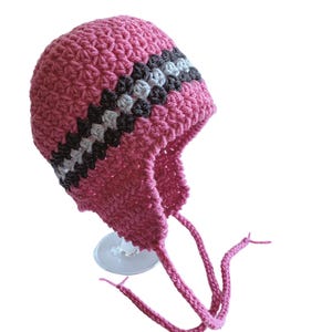 May include: Pink crocheted hat with a gray and black striped band. The hat has ear flaps and ties that can be tied under the chin.