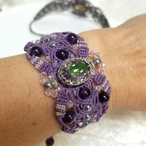 Peut inclure: Bracelet macramé fait main de couleur violette, orné d'une pierre verte ovale et de petites perles violettes et argentées. Le bracelet est orné de pierres d'améthyste et de nœuds complexes.