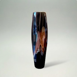 Può includere: Un vaso alto e scuro con finitura lucida. Il vaso ha una base nera che sfuma in un marrone scuro e presenta un motivo unico di accenti arancioni, marroni e argentati. È un oggetto decorativo per la casa.