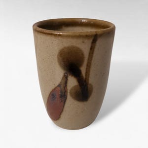 May include: A handmade ceramic tumbler with a beige speckled finish. The tumbler features abstract brown and reddish-brown painted designs. The rim and interior have a darker brown glaze. This unique piece is perfect for enjoying your favorite beverages.
