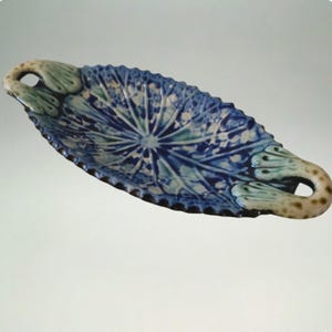 Può includere: Piatto da portata ovale in ceramica con motivo floreale blu e bianco. Il piatto ha un bordo smerlato e manici con un design verde e beige. Il piatto misura circa 30 cm di lunghezza.