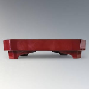 以下が含まれることがあります： 光沢のある仕上げの、長方形の赤い漆塗りの木製トレイ。 トレイは4つの短い脚で支えられています。 デザインはシンプルでエレガントで、サービングやディスプレイに適しています。