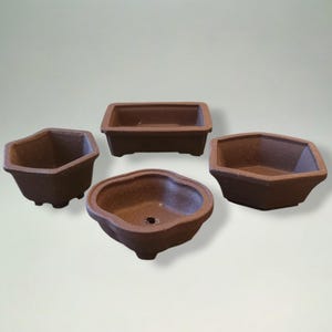 Puede incluir: Cuatro macetas de bonsái de cerámica marrón de varias formas: rectangular, hexagonal y redondeada. Las macetas tienen una superficie texturizada y están diseñadas para plantar árboles o arbustos pequeños. Ideal para un jardín en miniatura.
