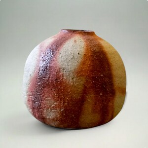 May include: A handmade ceramic vase with a rounded form and a small opening. The vase has a textured surface with a colour palette of white, reddish-brown, and tan. The design features vertical streaks of colour.