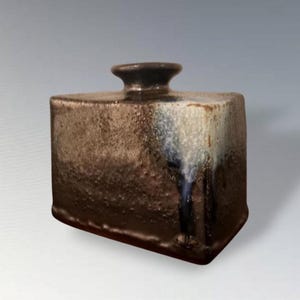 May include: A square, ceramic vase with a textured, mottled brown surface. The vase has a small, dark brown neck and a base that is slightly darker than the body. The glaze has streaks of white and blue.