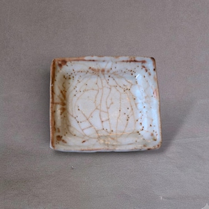 May include: A square ceramic dish featuring a glossy off-white glaze with a prominent brown crackle pattern across the surface. The edges of the dish are finished with a darker brown rim, and the overall texture appears smooth and reflective.