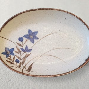 Puede incluir: Una taza de cerámica blanca con asa negra y el texto "But First, Coffee" en negro, con una fuente de estilo manuscrito. La taza está sobre una superficie blanca.