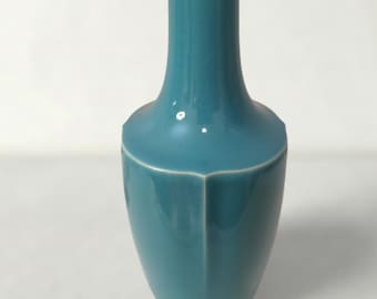 May include: A teal-colored ceramic vase with a unique, angular design. The vase has a long, slender neck and a wider, faceted body. The glossy finish reflects light, highlighting the smooth curves and sharp angles of the piece. A decorative item for the home.
