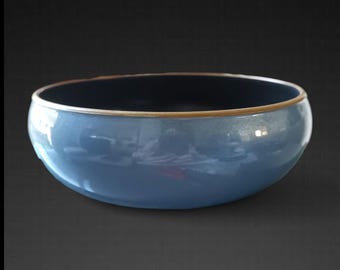 Puede incluir: Un cuenco de cerámica azul brillante con interior oscuro y borde dorado. El cuenco tiene forma redondeada y refleja la luz, creando reflejos en su superficie. El diseño es simple y elegante.