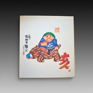 May include: A square white print featuring a colorful illustration of a smiling figure in a green hat and blue jacket riding a brown boar with white markings. The print includes Japanese text, red stamps, and a large red character on the bottom right.