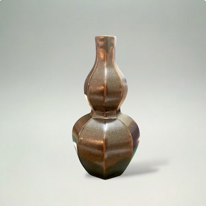 May include: A brown, double-gourd-shaped vase with a metallic finish. The vase has a narrow neck and a wider, rounded base, with a faceted design. The overall height is approximately 8 inches.