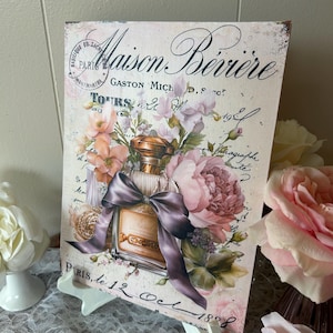 May include: A vintage-style rectangular canvas print featuring a perfume bottle with a large purple bow, surrounded by pink and peach flowers. The print has faded text and script, with the words "Maison Bévère" visible.