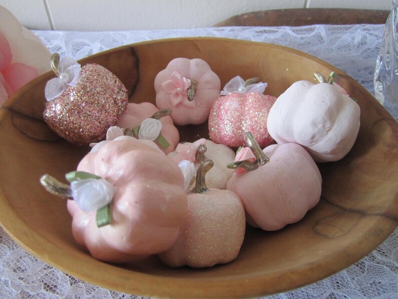 Pode incluir: Uma tigela de madeira cheia de ab&oacute;boras rosa decorativas. Algumas s&atilde;o lisas, outras com glitter. V&aacute;rias t&ecirc;m pequenos detalhes em tecido e caules. As ab&oacute;boras variam em tamanho e forma.