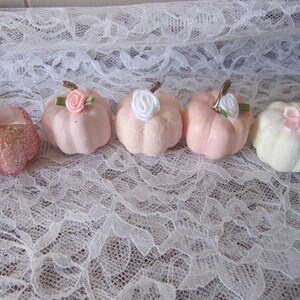 Pode incluir: Cinco ab&oacute;boras decorativas em tons de rosa e branco, cada uma com um caule dourado e uma flor ou la&ccedil;o de tecido. Uma ab&oacute;bora &eacute; coberta com glitter rosa. As ab&oacute;boras est&atilde;o dispostas sobre uma superf&iacute;cie de renda branca.