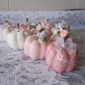 Pode incluir: Uma cole&ccedil;&atilde;o de pequenas ab&oacute;boras decorativas em tons de rosa e branco. Algumas ab&oacute;boras s&atilde;o cobertas de glitter, enquanto outras t&ecirc;m um acabamento liso. Cada ab&oacute;bora &eacute; adornada com uma pequena flor e um caule.