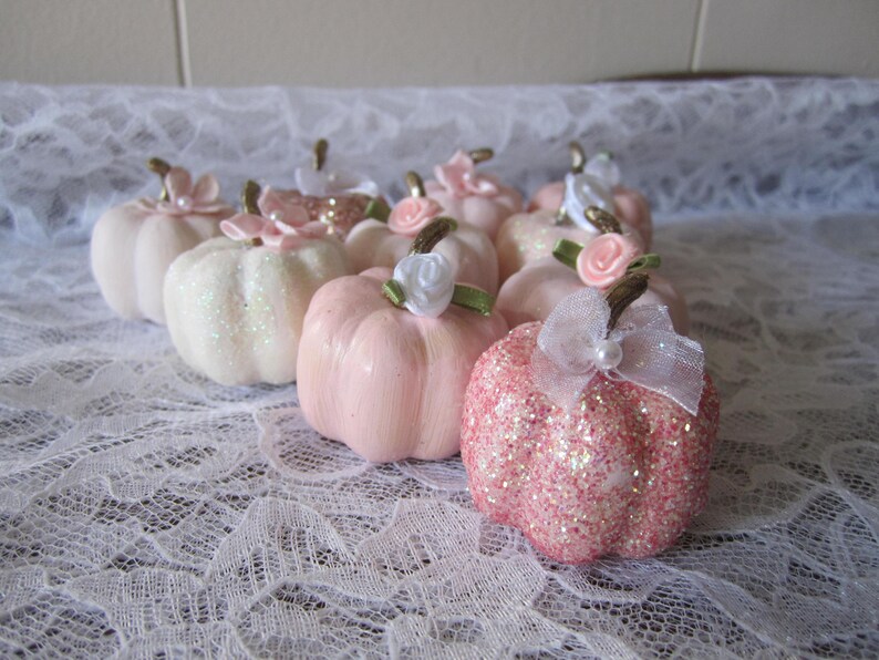 Pode incluir: Uma cole&ccedil;&atilde;o de pequenas ab&oacute;boras decorativas em tons de rosa e branco. Algumas ab&oacute;boras s&atilde;o cobertas de glitter, enquanto outras t&ecirc;m um acabamento liso. Cada ab&oacute;bora &eacute; adornada com uma pequena flor e um caule.