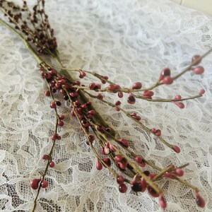 May include: A decorative floral spray featuring multiple thin, brown, wire-wrapped stems adorned with small, glossy, teardrop-shaped berries in shades of deep red and muted pink, arranged in a cluster that branches out into several slender twigs.