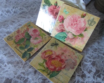 May include: Four square decorative coasters with floral designs. Each coaster features a different arrangement of pink roses, hydrangeas, and other flowers on a cream-colored background. Some coasters have a butterfly or bee accent.