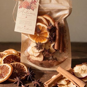 Könnte beinhalten: Ein durchsichtiger Beutel gefüllt mit getrockneten Orangenscheiben, Apfelscheiben, Zimtstangen und Sternanis. Ein mit Bindfaden befestigtes Etikett trägt die Aufschrift Autumn AT HOME SIMMERING POTPOURRI und Velvet Tumbleweed.