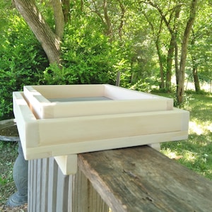 May include: Two wooden frames stacked on top of each other. The frames are made of unfinished light wood and are rectangular in shape. The frames are sitting on a weathered wooden surface.