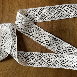 May include: White crochet lace trim with a delicate floral pattern. The lace is approximately 1 inch wide and has a soft, delicate texture.