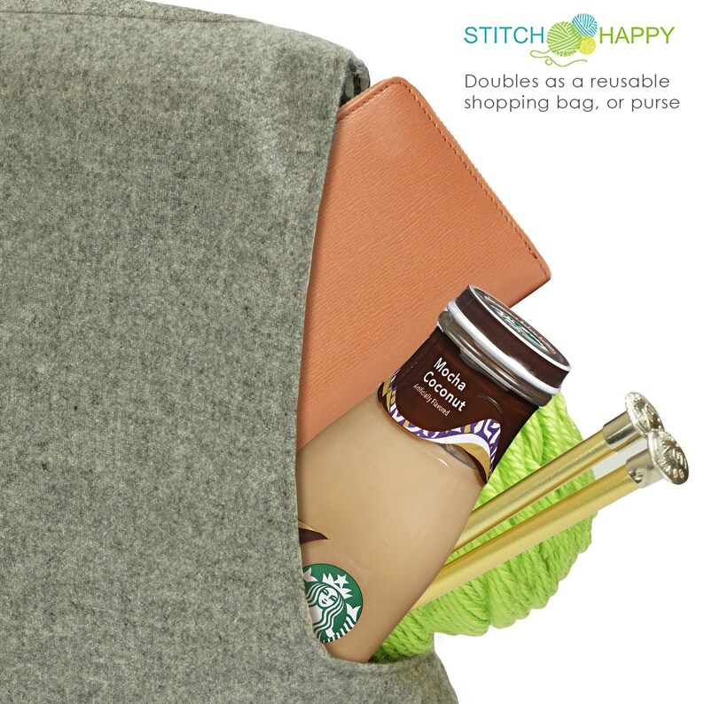 May include: A gray felt tote bag with a brown leather-like flap. The bag is filled with a bottle of Mocha Coconut flavored coffee, green yarn, and two gold knitting needles. The bag has the text "STITCH HAPPY" and "Doubles as a reusable shopping bag, or purse" printed on the front.