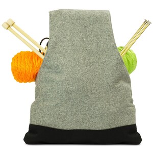 May include: Gray knitting bag with a black bottom. The bag is filled with two balls of yarn, one orange and one green, and knitting needles.