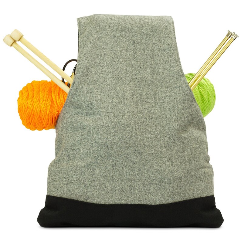 May include: Gray knitting bag with a black bottom. The bag is filled with two balls of yarn, one orange and one green, and knitting needles.