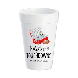 May include: White foam cup with a red cooler, two bottles of beer, and a football. The text on the cup reads "Tailgates & Touchdowns with the Campbells".