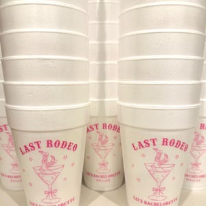 May include: White styrofoam cups with pink text and a pink graphic of a martini glass with a cowboy boot in it. The text on the cups reads "Last Rodeo" and "Liz's Bachelorette Dallas".