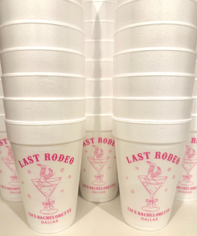 May include: White styrofoam cups with pink text and a pink graphic of a martini glass with a cowboy boot in it. The text on the cups reads "Last Rodeo" and "Liz's Bachelorette Dallas".