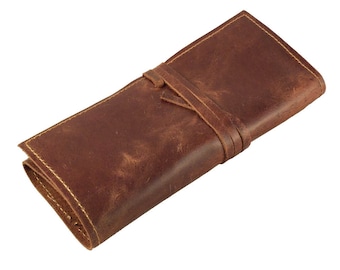 May include: A brown leather pencil case with a strap closure. The case is made of distressed leather and has a rustic look.