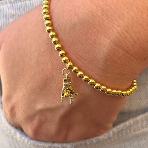 May include: A gold beaded bracelet with a gold charm shaped like a hand making the rock and roll hand gesture.