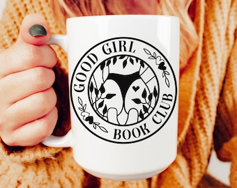 Può includere: Tazza in ceramica bianca con un design grafico in bianco e nero che dice "Good Girl Book Club" in un cerchio con un'immagine stilizzata di gambe di donna e un motivo floreale.