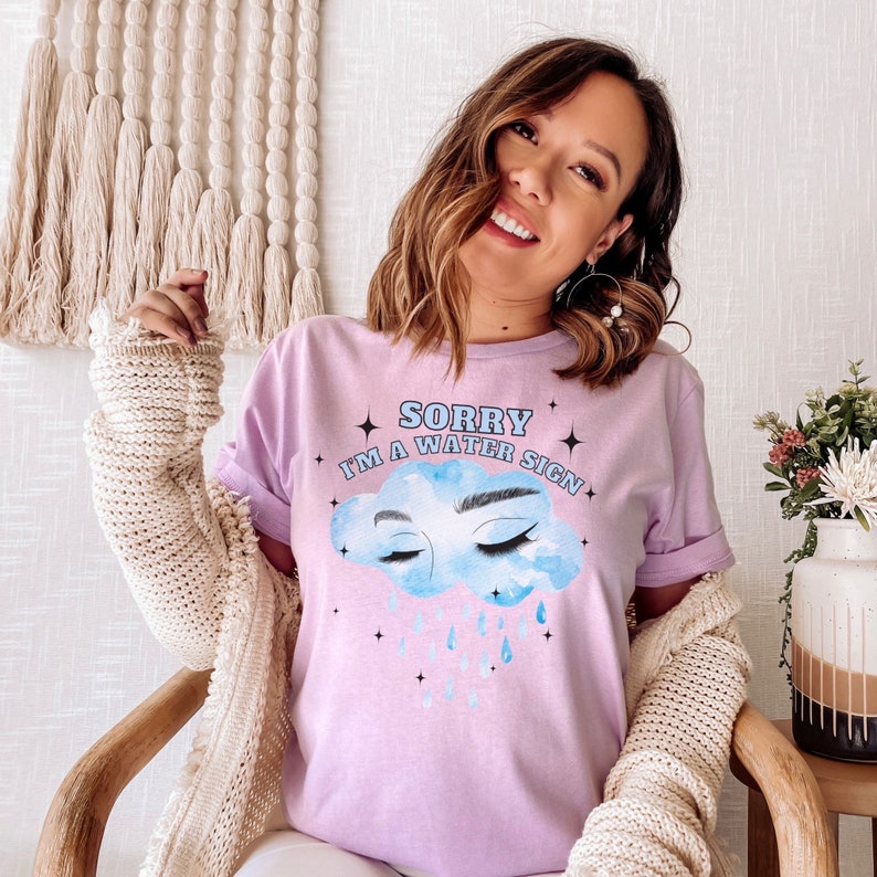 May include: A pink t-shirt with a blue cloud graphic and the text "Sorry I'm a water sign". The cloud has eyes and eyelashes and is raining blue raindrops.