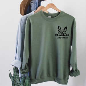 May include: A green sweatshirt with a black graphic of a French bulldog peeking over the top of the pocket. The text "Lolly's Mom" is printed below the graphic.