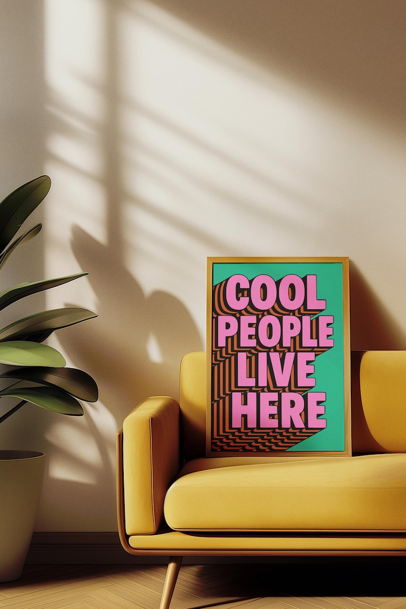 May include: A framed art print with the text "COOL PEOPLE LIVE HERE" in pink and orange, set against a teal background. The print is displayed on a yellow sofa, with a potted plant in the corner.