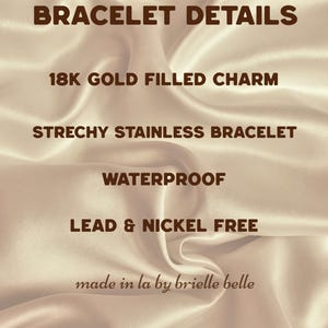 May include: Image with text: "BRACELET DETAILS", "18K GOLD FILLED CHARM", "STRECHY STAINLESS BRACELET", "WATERPROOF", "LEAD & NICKEL FREE", and "made in la by brielle belle". The background is a satin fabric.