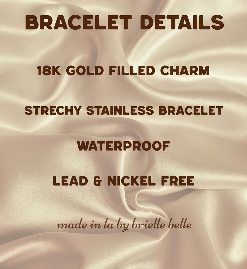 May include: Image with text: "BRACELET DETAILS", "18K GOLD FILLED CHARM", "STRECHY STAINLESS BRACELET", "WATERPROOF", "LEAD & NICKEL FREE", and "made in la by brielle belle". The background is a satin fabric.