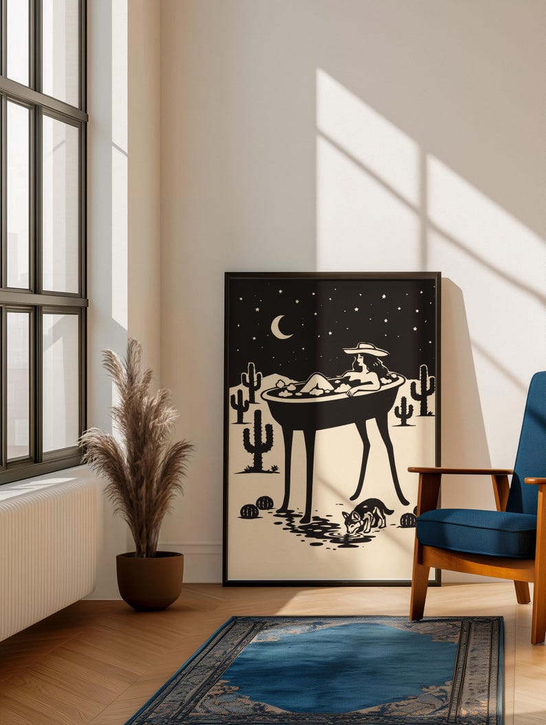 May include: Black and white art print depicting a person relaxing in a bathtub under a starry night sky with cacti. The print is framed and displayed in a room with a blue chair, a rug, and a potted plant.