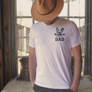 May include: A white t-shirt with a black French Bulldog peeking over the top and the text "Frenchie Dad" underneath.