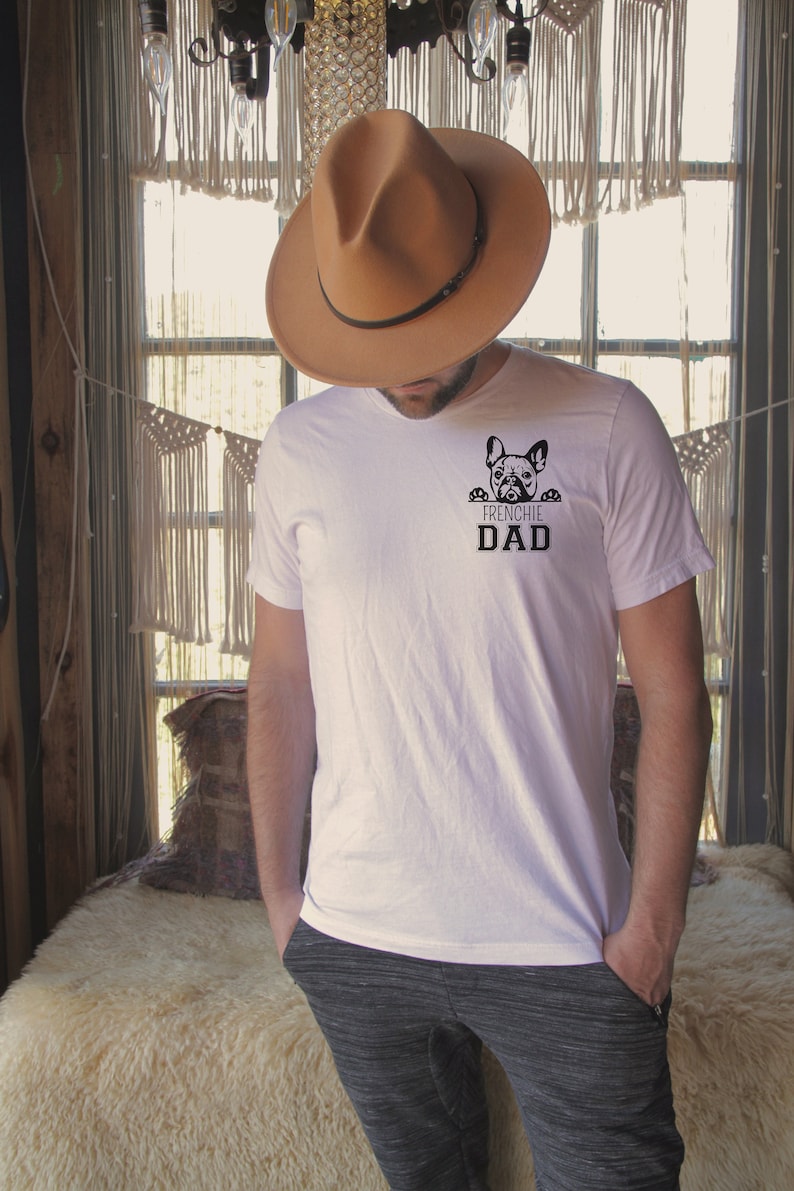 May include: A white t-shirt with a black French Bulldog peeking over the top and the text "Frenchie Dad" underneath.