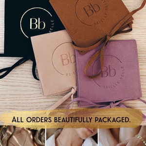 May include: An assortment of jewelry packaging in black, tan, blush, and purple. Each package has a debossed logo and the words "Brielle Belle". A gold bracelet with smiley faces is visible. The text "ALL ORDERS BEAUTIFULLY PACKAGED" is also present.