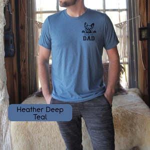 May include: A heather deep teal t-shirt with a French bulldog peeking out from the pocket and the text "Frenchie Dad".