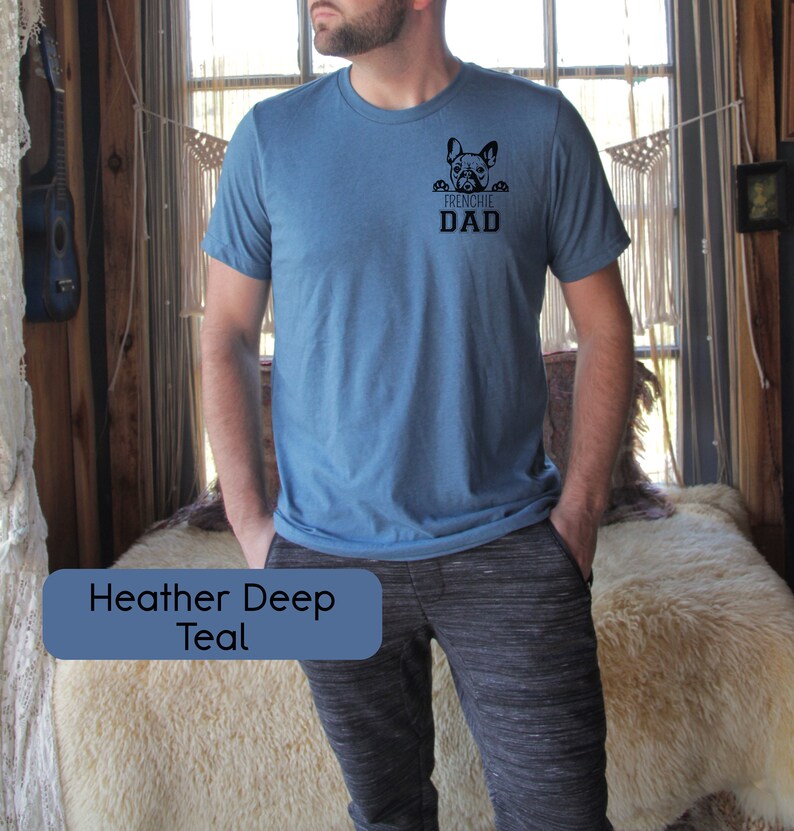 May include: A heather deep teal t-shirt with a French bulldog peeking out from the pocket and the text "Frenchie Dad".