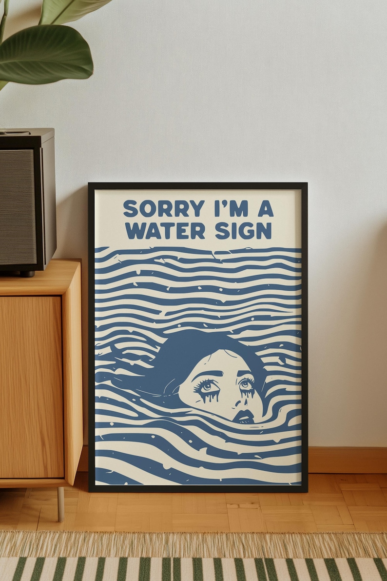 May include: A framed art print featuring a stylized illustration of a person submerged in water. The artwork is in shades of blue and cream, with the text "SORRY I'M A WATER SIGN" at the top. The person's face is visible, with eyes looking upwards.