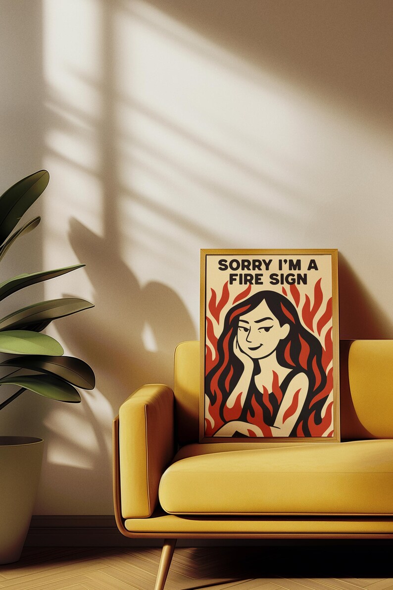 May include: A framed art print with the text "SORRY I'M A FIRE SIGN" features a woman with red hair and flames. The artwork is set against a cream background with a yellow sofa and a potted plant.