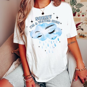 May include: White t-shirt with a blue cloud graphic and the text "Sorry I'm a water sign".