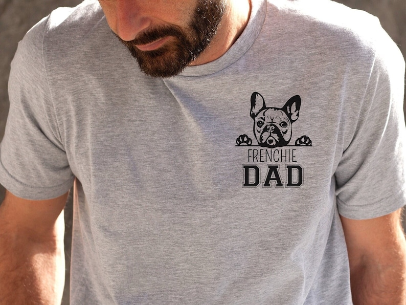 May include: A gray t-shirt with a black graphic of a French bulldog peeking over a sign that says "Frenchie Dad".