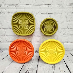 May include: Four vintage plastic lids in shades of green, orange, and yellow. The lids have a radial design with a central circle and are square and round. The lids are on a white and gray surface.